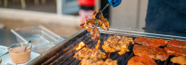 Cooking chicken on a barbecue using tongs to handle food safely